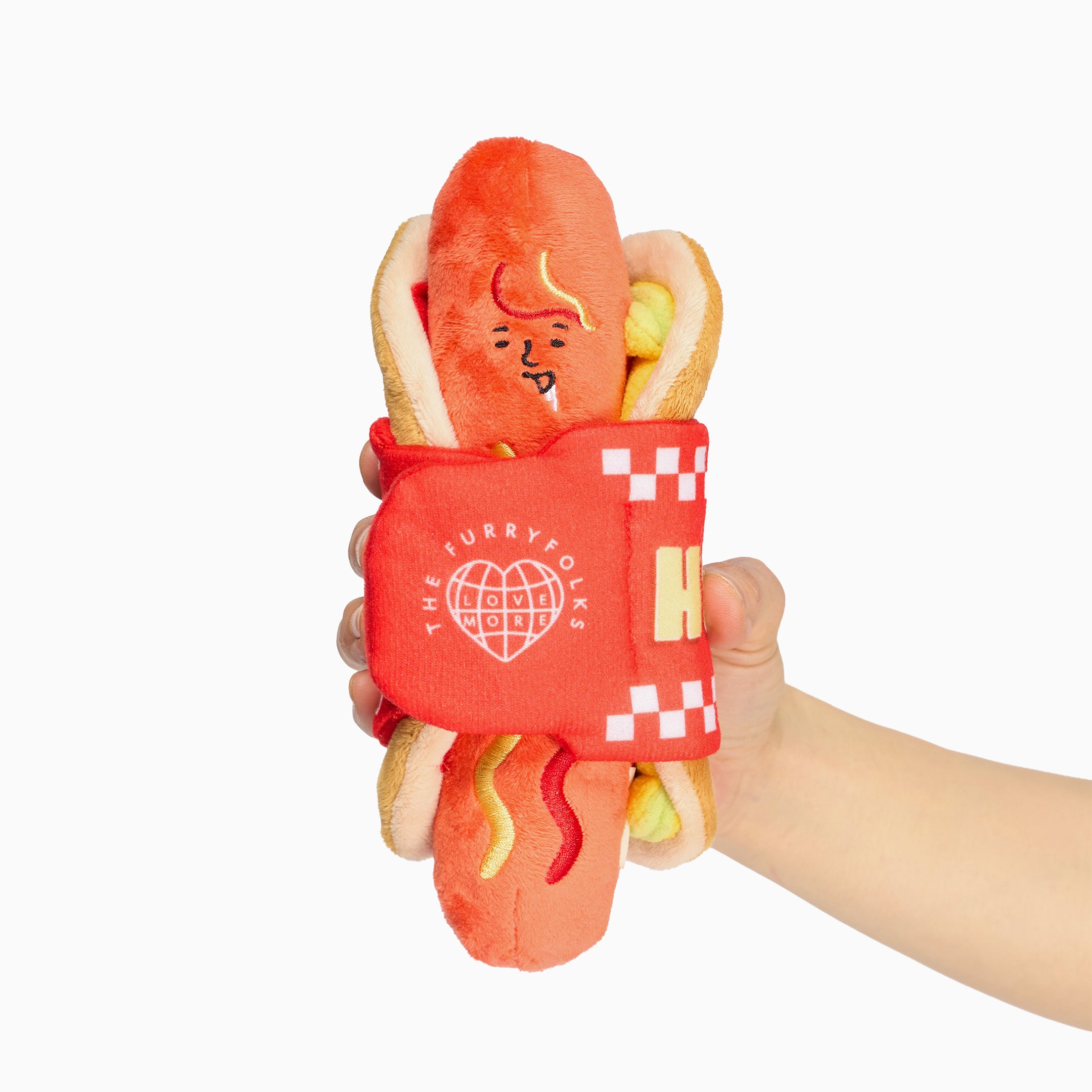 Jouet de fouille Le Hot Dog en peluche avec son pain, sa moutarde et son ketchup, tenu à la main