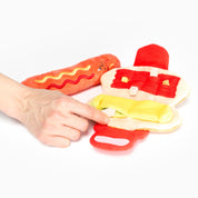 Jouet de fouille Le Hot Dog rouge et jaune avec son pain, tenu à la main sur fond blanc
