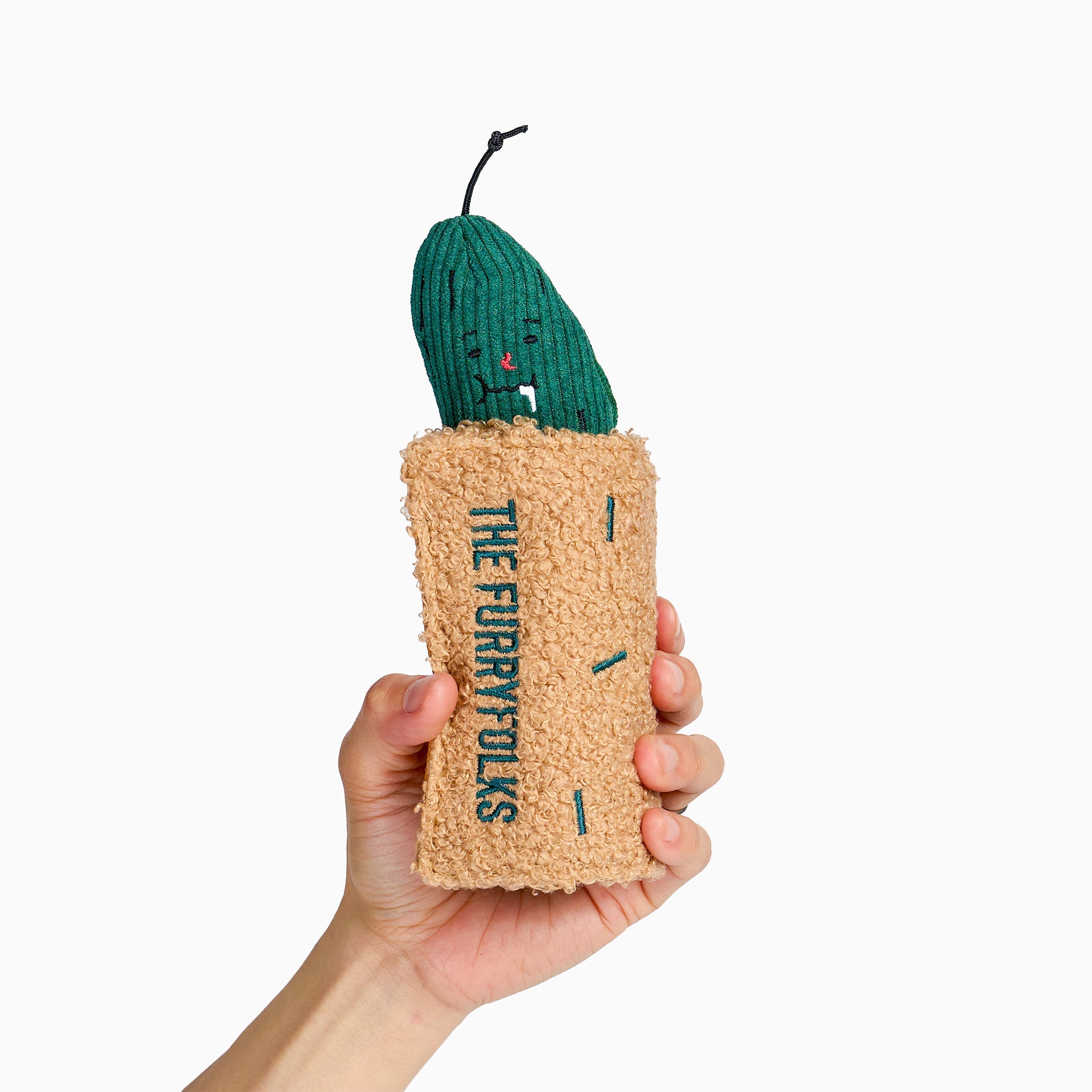 Jouet de fouille Le cornichon : cornichon vert souriant dans son enveloppe beige tenu à la main