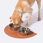 Un chien mange dans ses gamelles sur un tapis pour gamelle de chiens orange